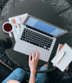 A person works on a laptop at a kitchen table next to a coffee mug.
